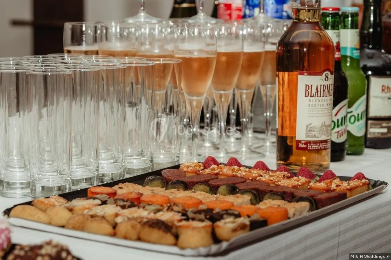 Plateau de bouchées variées devant des verres à pied remplis de boisson pétillante et une bouteille de whisky.