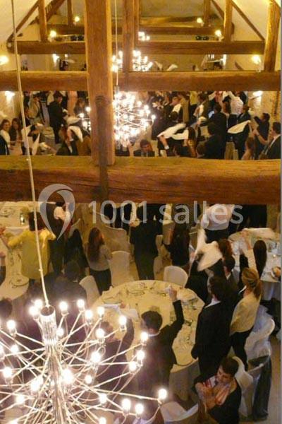 Salle de réception avec des invités debout autour de tables dressées, sous des lustres modernes et une charpente apparente.
