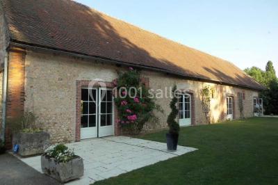 Façade d'un bâtiment en pierre éclairée la nuit, avec des portes vitrées et des chaises disposées sur une pelouse.