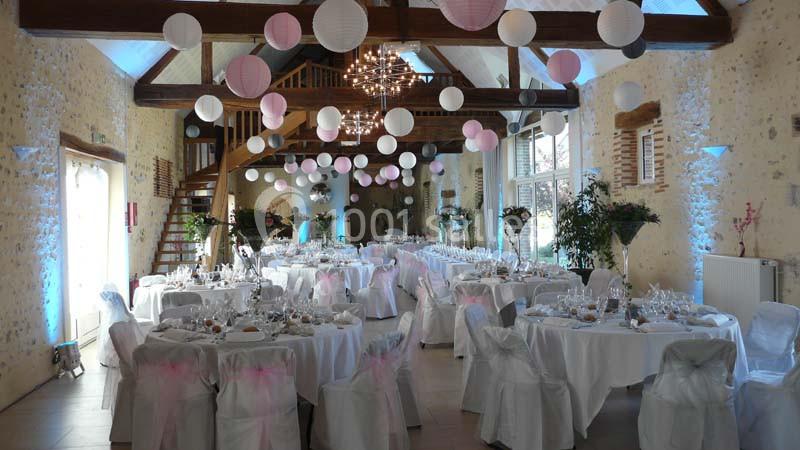 Salle de réception décorée avec des tables dressées, des chaises blanches et des lanternes suspendues au plafond.