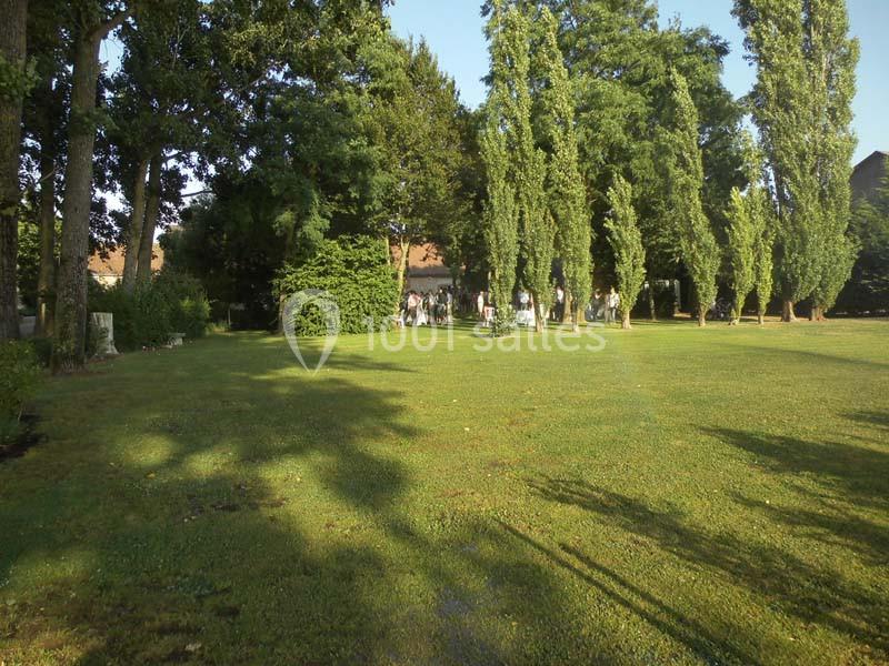 Pelouse verdoyante bordée d'arbres, avec des personnes rassemblées à l'ombre en arrière-plan.