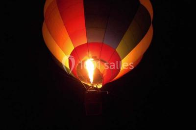 Façade d'un bâtiment en pierre éclairée la nuit, avec des portes vitrées et des chaises disposées sur une pelouse.
