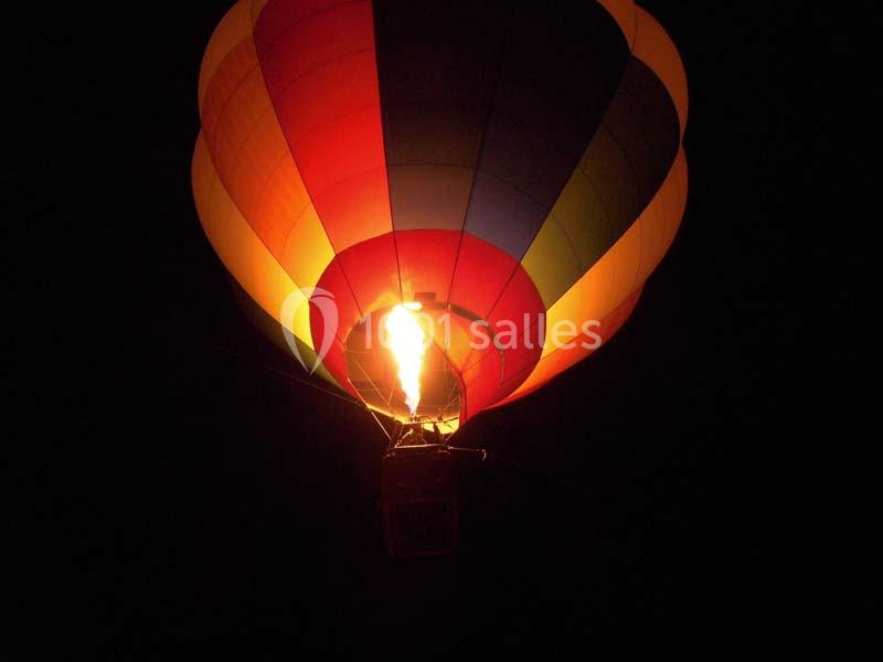 Montgolfière colorée illuminée par son brûleur, flottant dans le ciel nocturne.