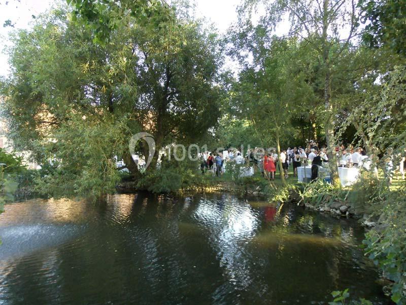 Un étang entouré de végétation avec un groupe de personnes rassemblées dans un jardin en arrière-plan.
