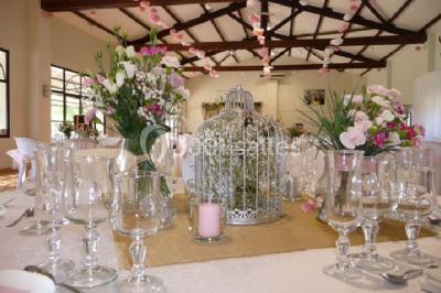 Salle de réception décorée avec des nappes blanches et des rubans rouges, tables ornées de centres de table fleuris.