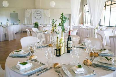 Salle de réception décorée avec des nappes blanches et des rubans rouges, tables ornées de centres de table fleuris.