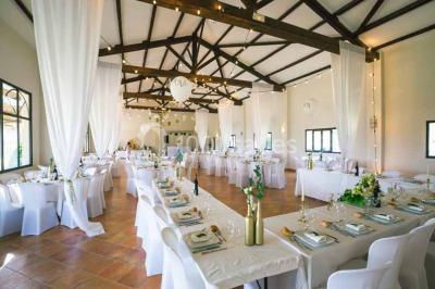 Salle de réception décorée avec des nappes blanches et des rubans rouges, tables ornées de centres de table fleuris.