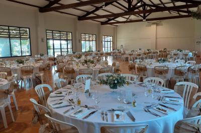 Salle de réception décorée avec des nappes blanches et des rubans rouges, tables ornées de centres de table fleuris.