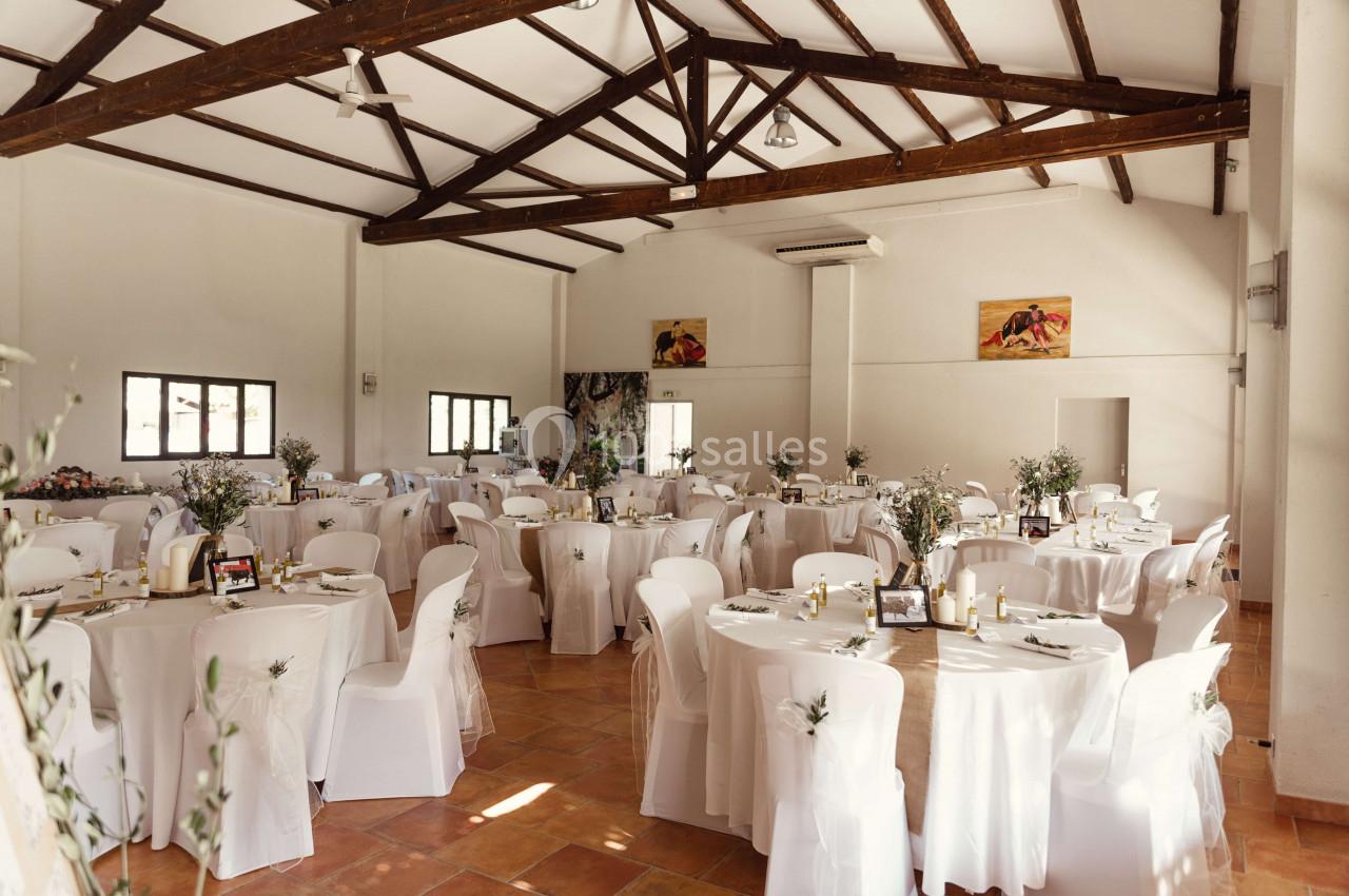 Salle de réception lumineuse avec des tables rondes décorées de nappes blanches et de centres de table floraux.