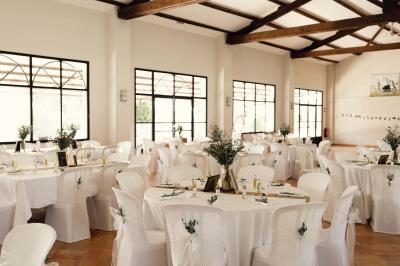 Salle de réception décorée avec des nappes blanches et des rubans rouges, tables ornées de centres de table fleuris.
