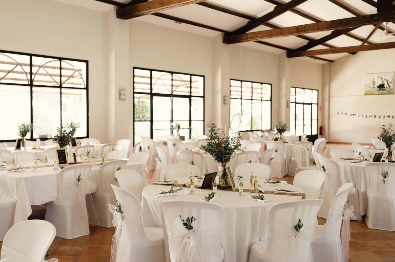 Salle de réception lumineuse avec des tables rondes décorées de nappes blanches, centres de table et chaises assorties.