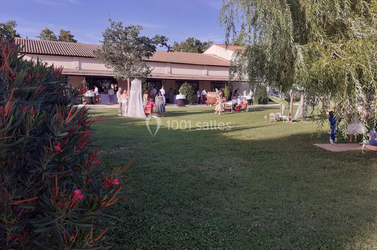 Jardin verdoyant avec des invités rassemblés près d'un bâtiment lors d'un événement en plein air.