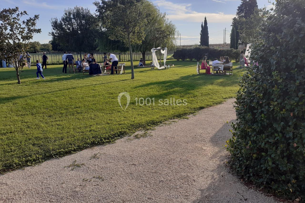 Des personnes se détendent et discutent dans un parc verdoyant avec des arbres, des tables et des structures blanches.
