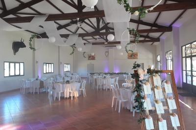 Salle de réception décorée avec des nappes blanches et des rubans rouges, tables ornées de centres de table fleuris.
