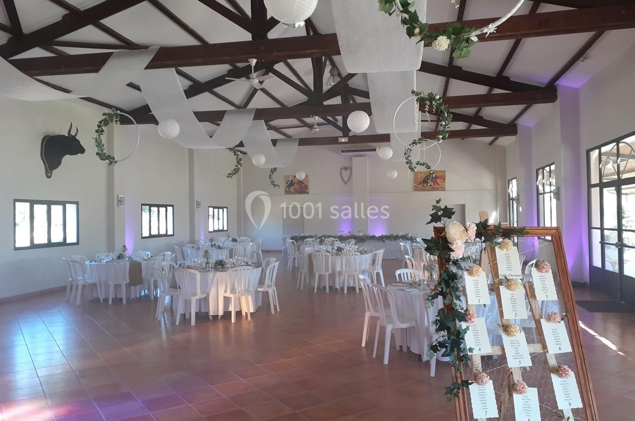 Salle de réception décorée pour un événement, avec tables dressées, guirlandes suspendues et plan de table fleuri.