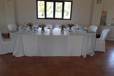 Salle de réception décorée avec des nappes blanches et des rubans rouges, tables ornées de centres de table fleuris.