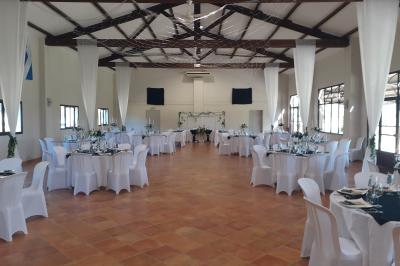 Salle de réception décorée avec des nappes blanches et des rubans rouges, tables ornées de centres de table fleuris.