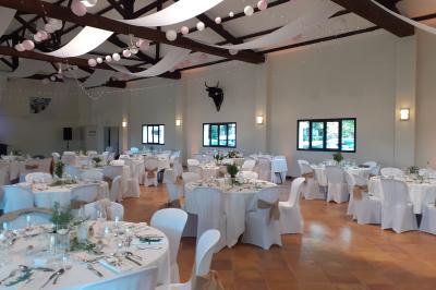 Salle de réception décorée avec des nappes blanches et des rubans rouges, tables ornées de centres de table fleuris.