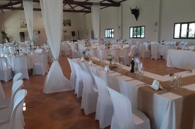 Salle de réception décorée avec des nappes blanches et des rubans rouges, tables ornées de centres de table fleuris.