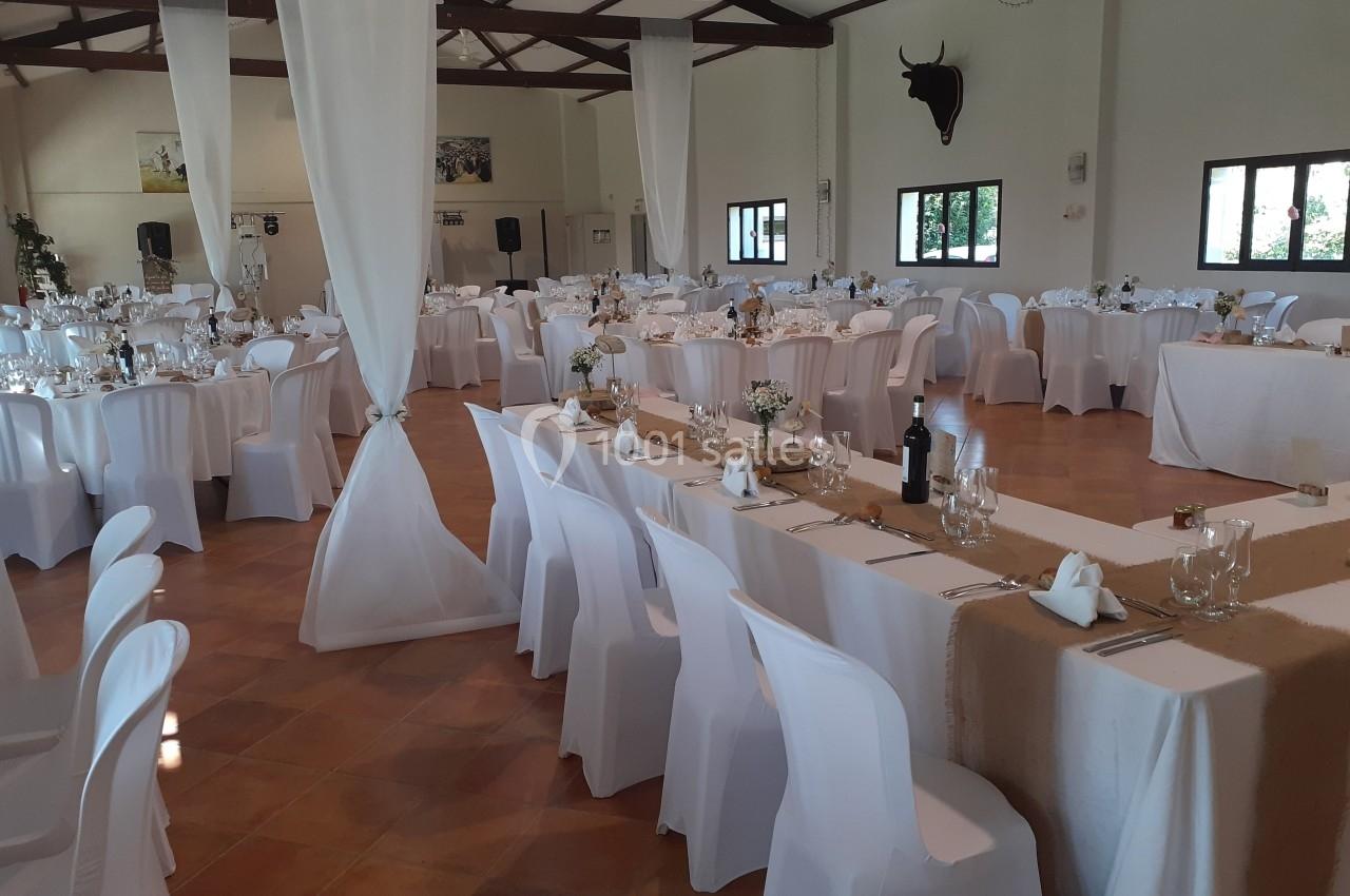Salle de réception décorée avec des tables rondes et rectangulaires, nappes blanches et chaises assorties.