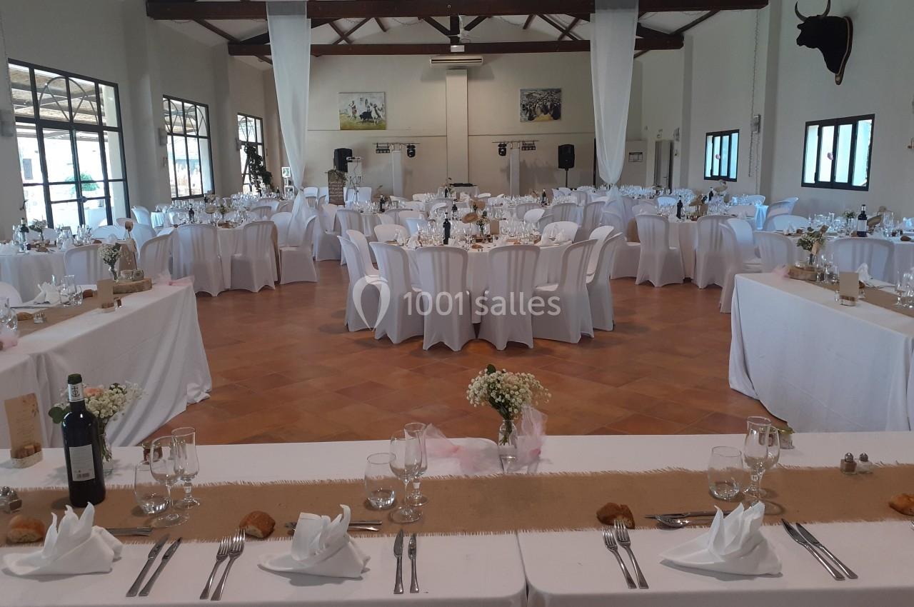 Salle de réception décorée pour un mariage, avec des tables rondes et rectangulaires dressées de nappes blanches.
