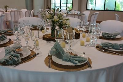 Salle de réception décorée avec des nappes blanches et des rubans rouges, tables ornées de centres de table fleuris.