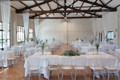Salle de réception décorée avec des nappes blanches et des rubans rouges, tables ornées de centres de table fleuris.
