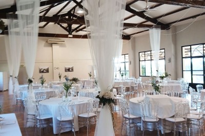 Salle de réception décorée avec des nappes blanches et des rubans rouges, tables ornées de centres de table fleuris.