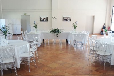 Salle de réception décorée avec des nappes blanches et des rubans rouges, tables ornées de centres de table fleuris.
