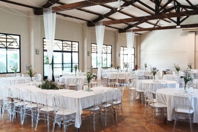 Salle de réception décorée avec des nappes blanches et des rubans rouges, tables ornées de centres de table fleuris.