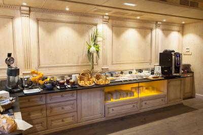 Buffet de petit-déjeuner avec viennoiseries, fruits, confitures, charcuterie et machine à café dans un décor en bois clair.