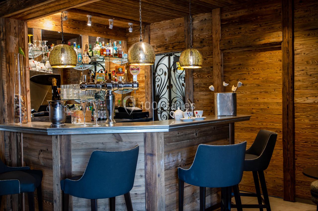 Bar en bois avec tabourets noirs, comptoir équipé de tireuses à bière, étagères garnies de bouteilles et lumières suspendues.