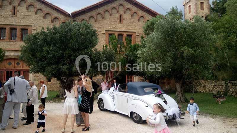 Un groupe de personnes rassemblé près d'une voiture ancienne blanche devant un bâtiment en pierre.