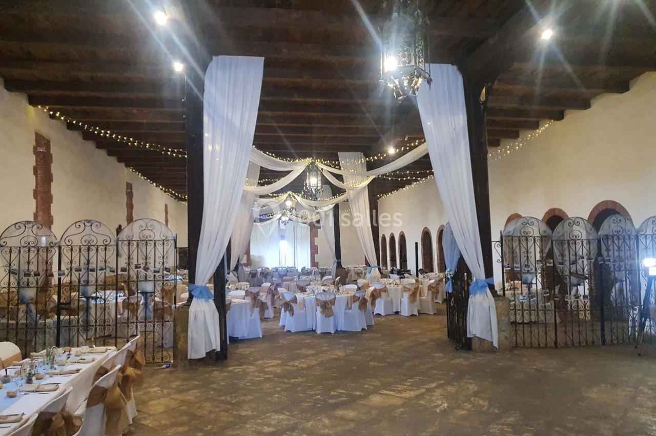Salle de réception décorée avec des tables dressées, des chaises ornées de nœuds et des drapés suspendus au plafond.