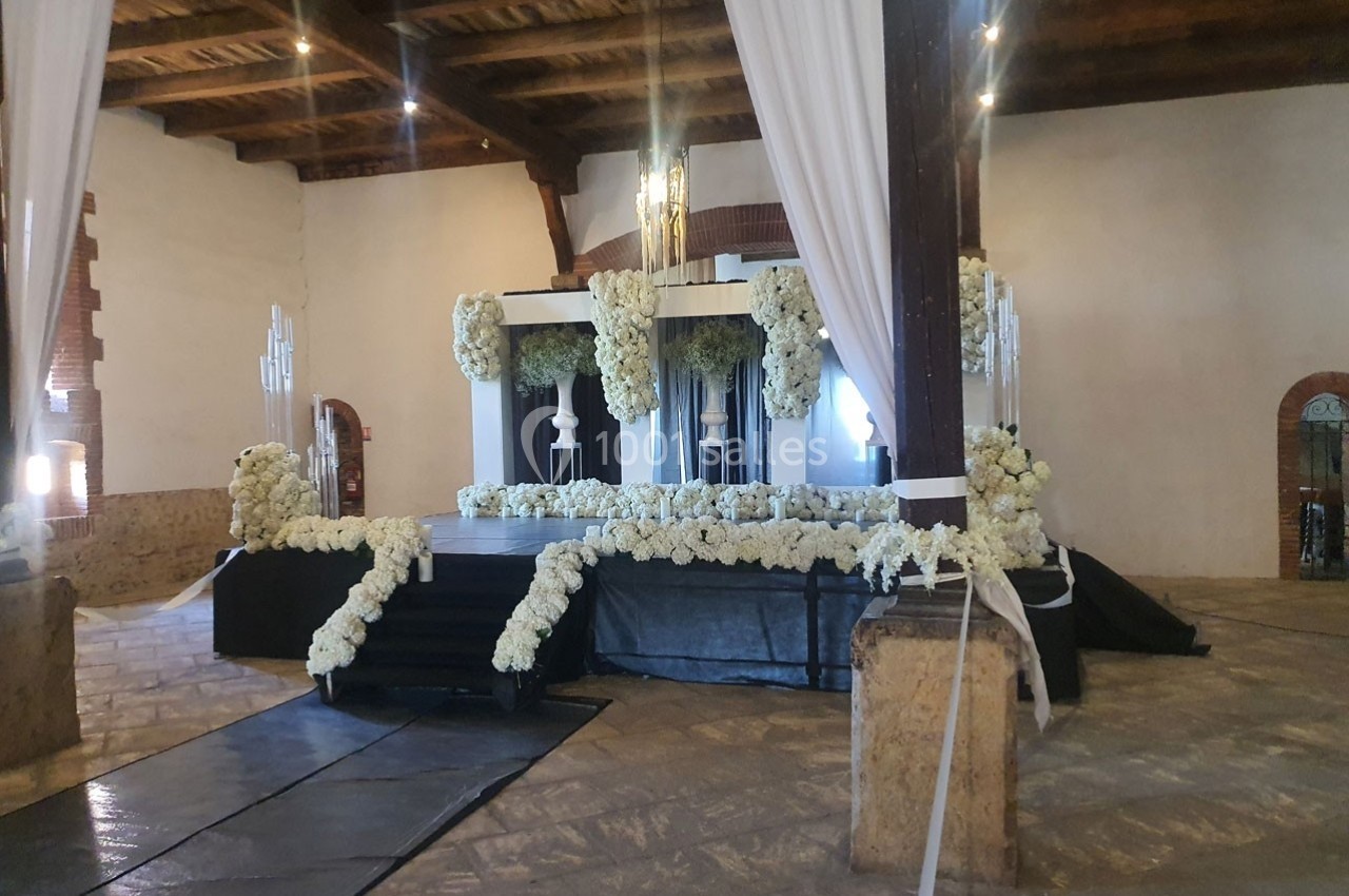 Scène décorée de fleurs blanches dans une salle avec plafond en bois et murs en pierre.