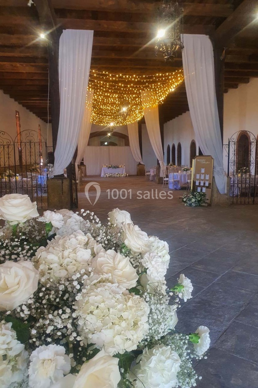 Salle de réception décorée avec des guirlandes lumineuses, des rideaux blancs et des arrangements floraux blancs au premier…