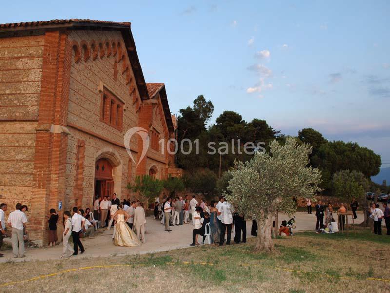 Groupe de personnes rassemblées devant un bâtiment en briques dans un cadre extérieur avec arbres et ciel dégagé.