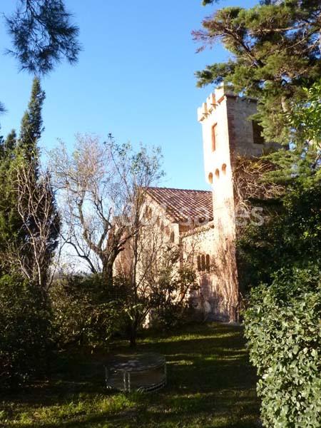 Église en pierre avec une tour, entourée de végétation et éclairée par une lumière naturelle sous un ciel bleu.