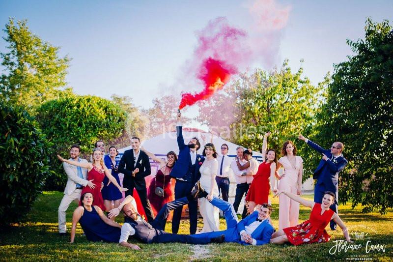 Un groupe de personnes posant de manière festive dans un jardin, avec une fumée rouge en arrière-plan.