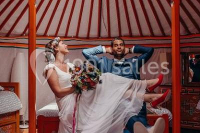 Une mariée en robe blanche applaudit devant un groupe de personnes dans un jardin lors d'une célébration.