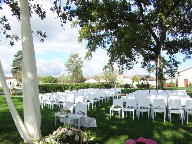 Chaises blanches alignées en extérieur sous des arbres, préparées pour une cérémonie avec des fleurs au premier plan.
