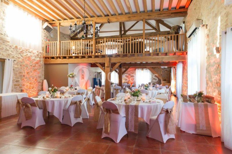 Salle de réception décorée avec des tables rondes, nappes blanches et chaises ornées de rubans beiges, dans un cadre…