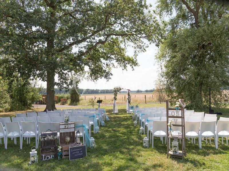 Chaises blanches alignées en extérieur sous des arbres, formant une allée menant à une arche de mariage décorée.