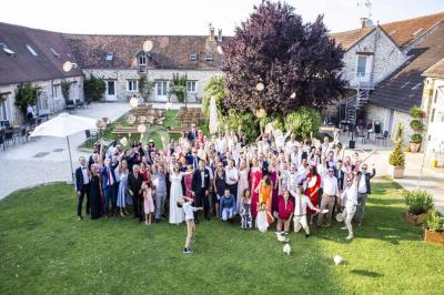 Une mariée en robe blanche applaudit devant un groupe de personnes dans un jardin lors d'une célébration.