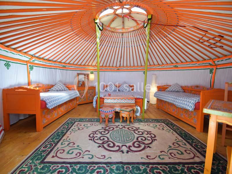 Intérieur d'une yourte colorée avec des lits en bois, un tapis orné et une table basse au centre.