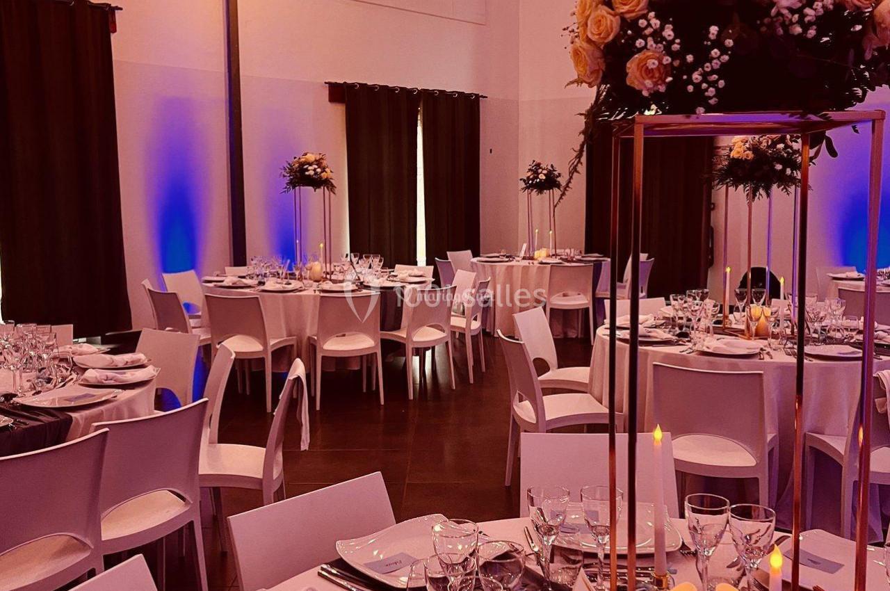Salle de réception décorée avec des tables élégantes, des chandelles, des fleurs et un éclairage chaleureux.