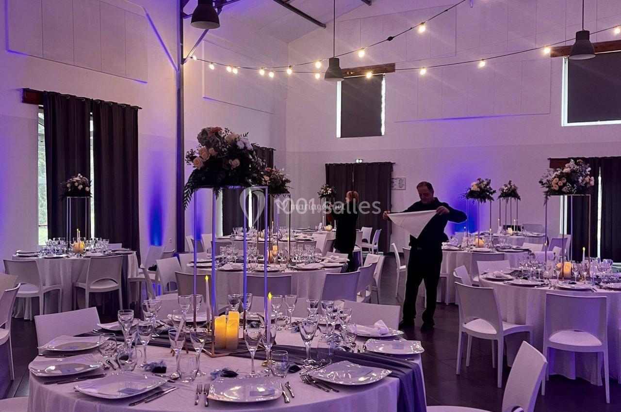 Salle de réception décorée avec des tables rondes dressées, éclairage tamisé et arrangements floraux élégants.