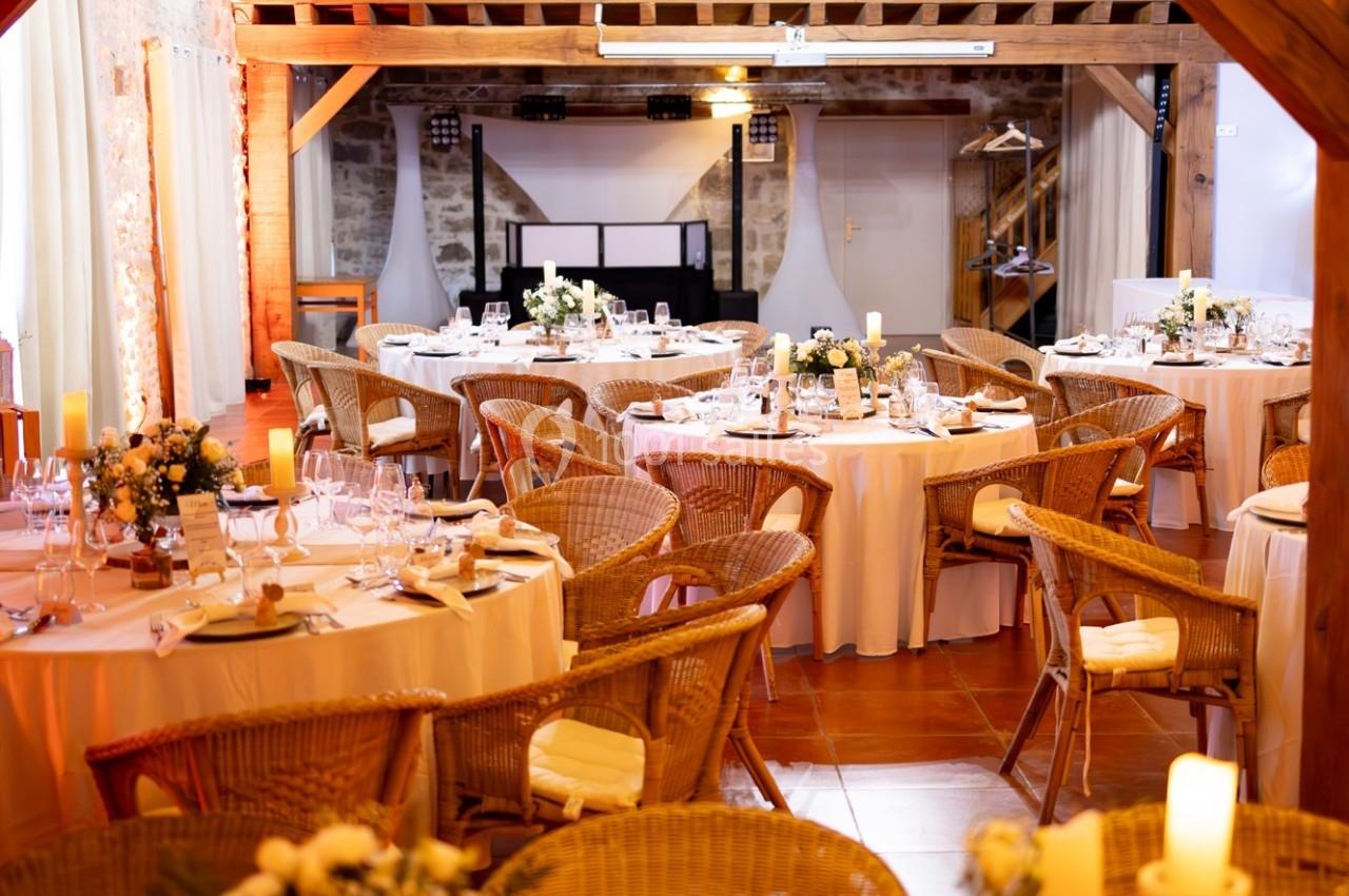 Salle de réception décorée avec des tables rondes, nappes blanches, chaises en osier et arrangements floraux.