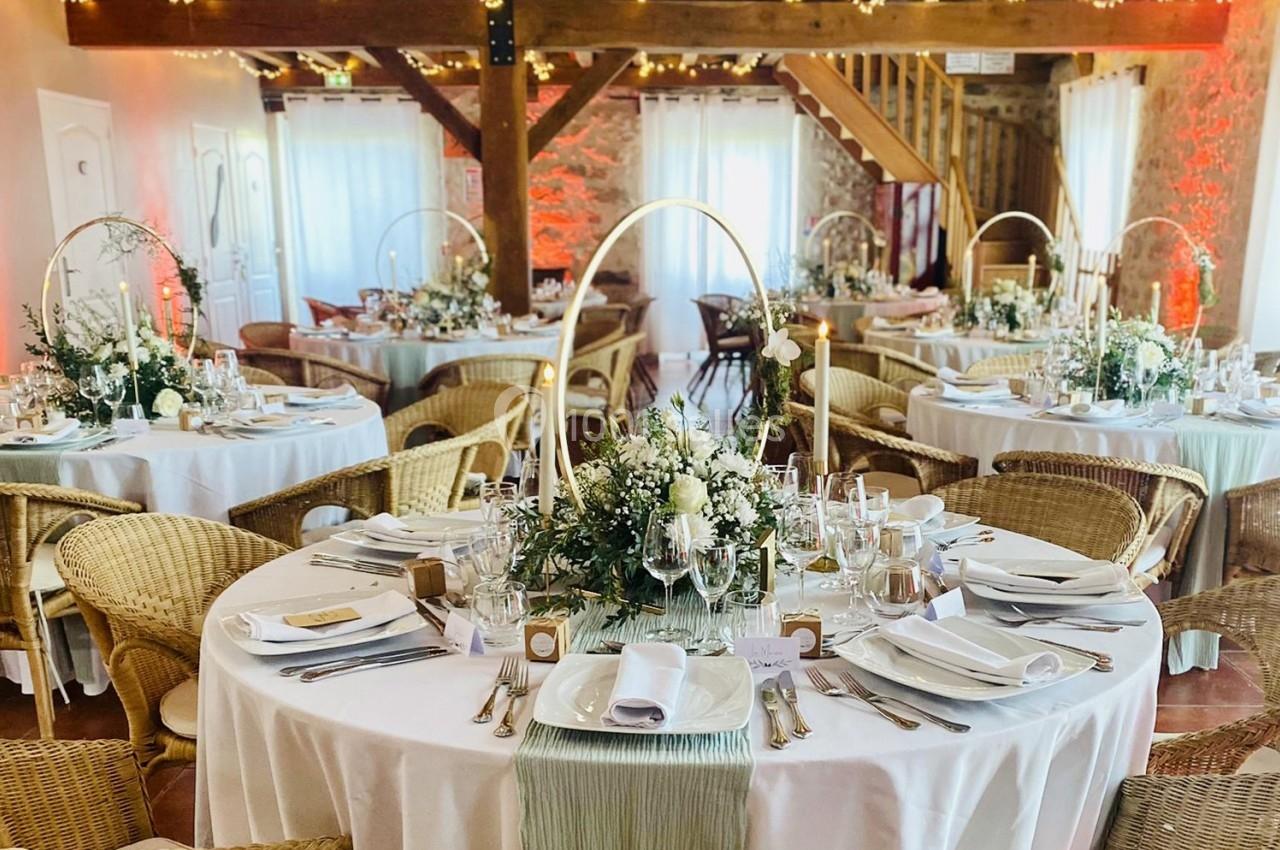 Salle de réception décorée avec des tables rondes, nappes blanches, compositions florales et bougies, ambiance chaleureuse.