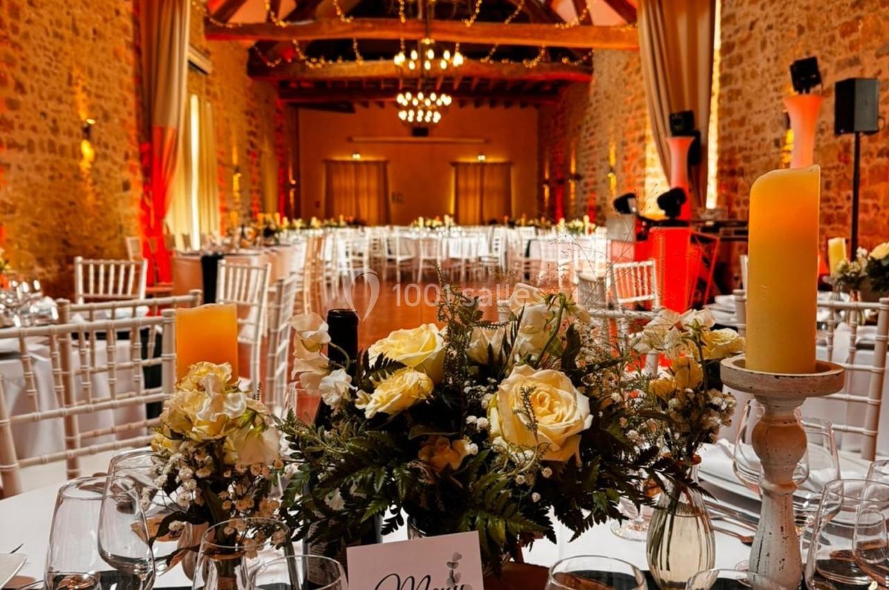 Salle de réception décorée avec des tables dressées, des chandeliers et des fleurs, dans un cadre en pierre avec poutres…